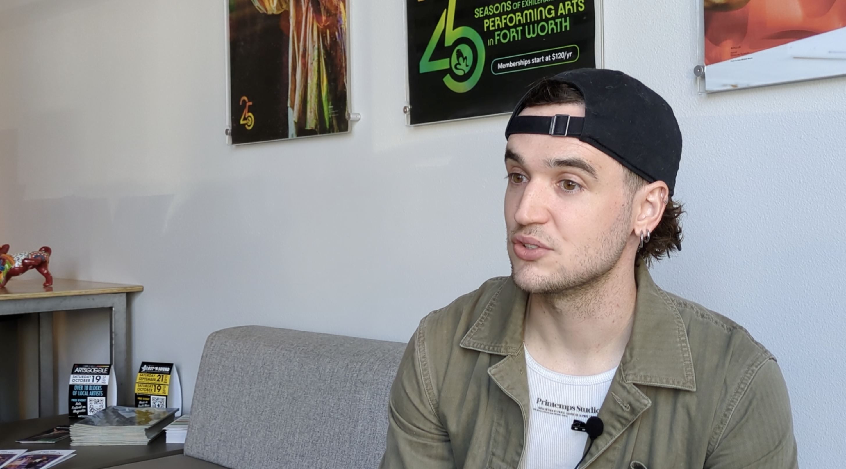 A young man sits with his cap turned backwards.