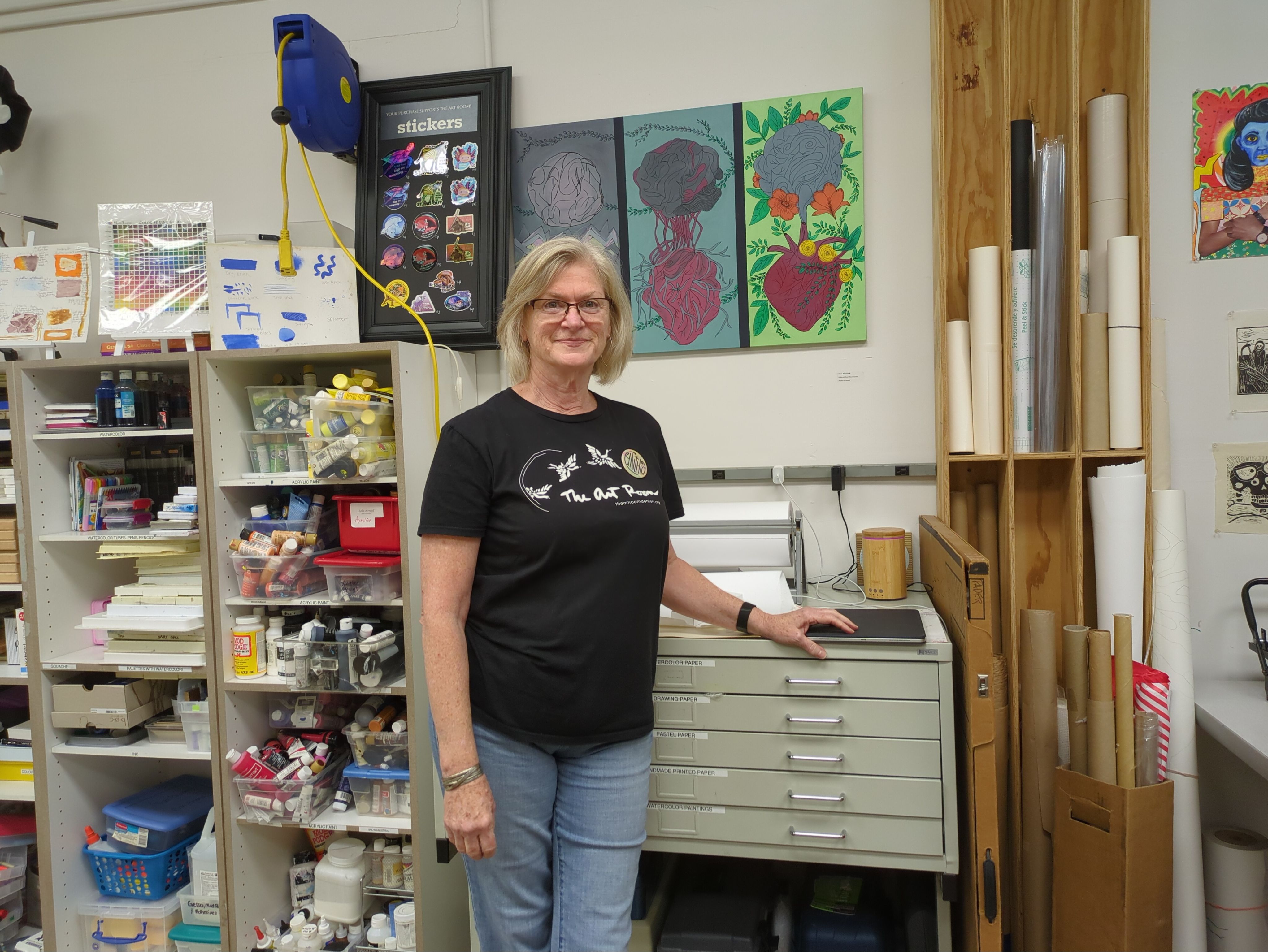 A woman stands in front of cabinets of art supplies.